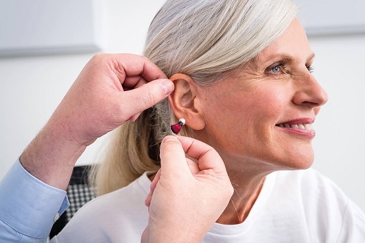 Hörgeräteakustiker passt älterer Frau ein modernes Hörgerät für besseres Hören an.